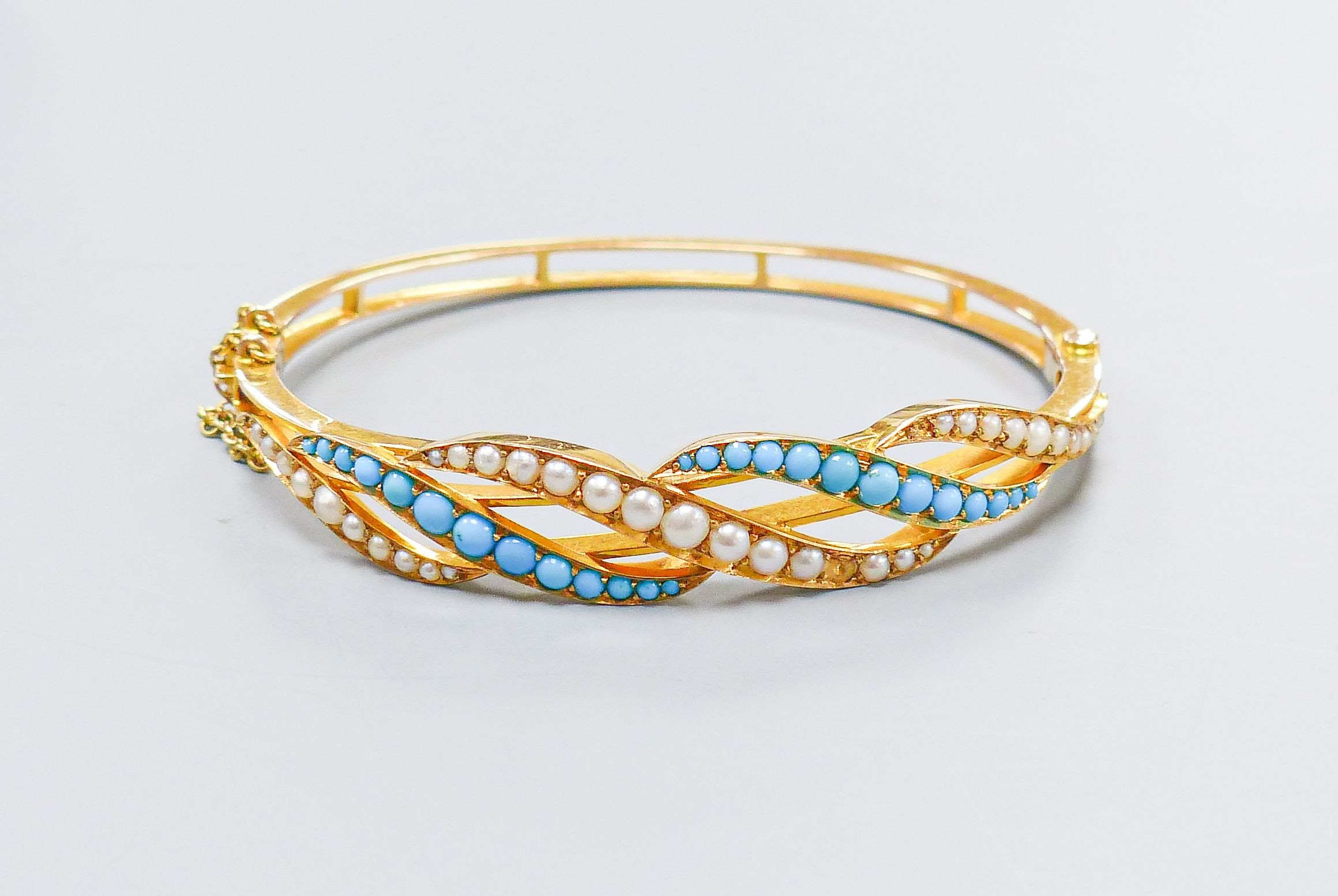 A boxed Edwardian yellow metal, graduated turquoise and seed pearl set hinged bangle, interior diameter 55mm, gross weight 15.5 grams.